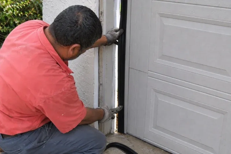 Gloved person holding a black strip along the side of a sectional garage-door opening — Garage Door Perimeter Weatherstrip, Scugog